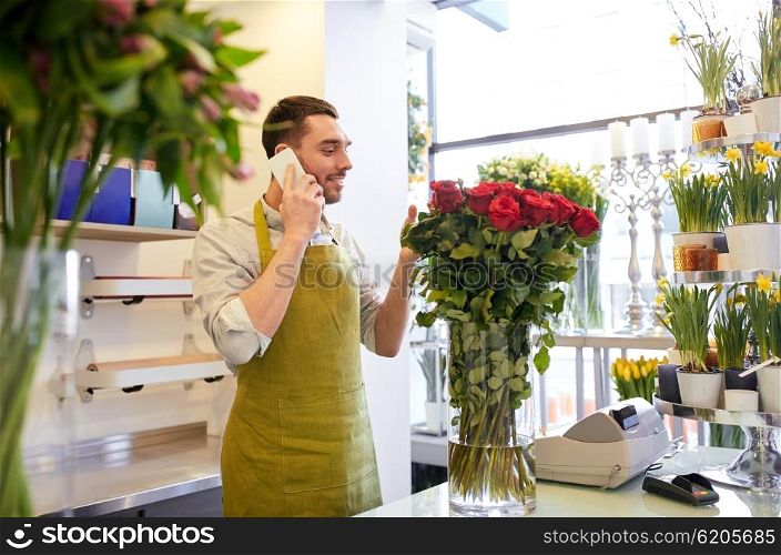people, sale, retail, business and floristry concept - florist man with red roses calling on smartphone at flower shop counter