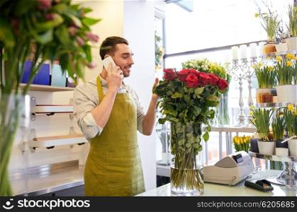 people, sale, retail, business and floristry concept - florist man with red roses calling on smartphone at flower shop counter