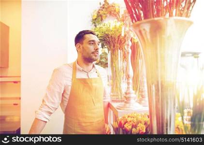 people, sale, retail, business and floristry concept - happy florist man with cashbox standing at flower shop. florist man or seller at flower shop