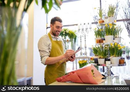 people, sale, retail, business and floristry concept - happy smiling florist man with bunch writing and making notes to clipboard at flower shop counter