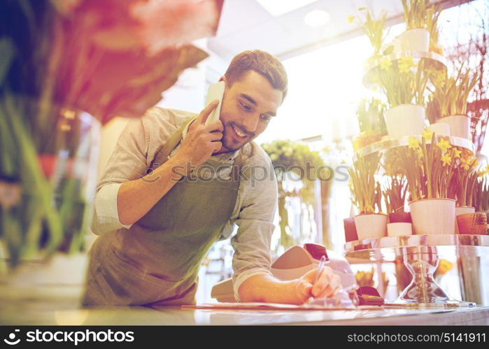 people, sale, retail, business and floristry concept - happy smiling florist man calling on smartphone and making notes to clipboard at flower shop counter. man with smartphone making notes at flower shop