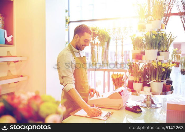 people, sale, retail, business and floristry concept - happy smiling florist man with clipboard and cashbox writing and making notes order at flower shop counter. florist man with clipboard at flower shop counter