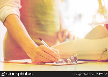 people, sale, retail, business and floristry concept - happy smiling florist man with clipboard and cashbox writing and making notes at flower shop counter. close up of man with clipboard at flower shop