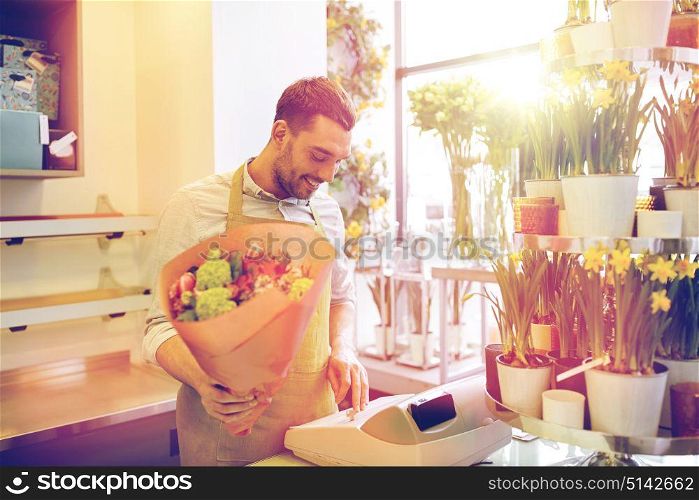 people, sale, retail, business and floristry concept - happy smiling florist man with bunch counting cost at flower shop cashbox. florist man or seller at flower shop cashbox