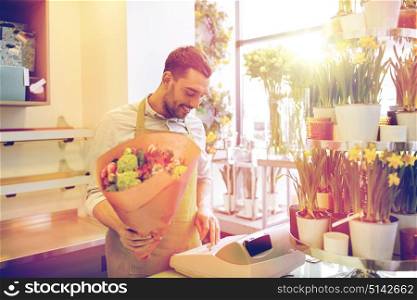 people, sale, retail, business and floristry concept - happy smiling florist man with bunch counting cost at flower shop cashbox. florist man or seller at flower shop cashbox
