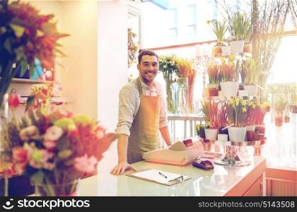 people, sale, retail, business and floristry concept - happy smiling florist man with clipboard and cashbox standing at flower shop counter. florist man with clipboard at flower shop counter
