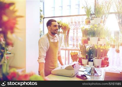 people, sale, retail, business and floristry concept - happy smiling florist man with cashbox standing at flower shop counter. florist man or seller at flower shop counter