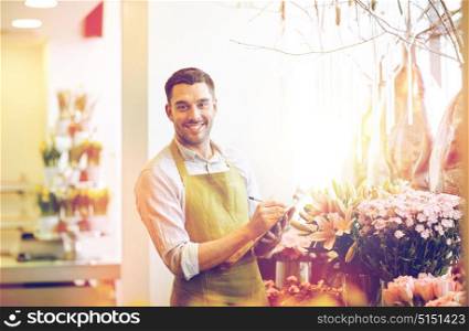 people, sale, retail, business and floristry concept - happy smiling florist man with clipboard writing and making notes order at flower shop. florist man with clipboard at flower shop
