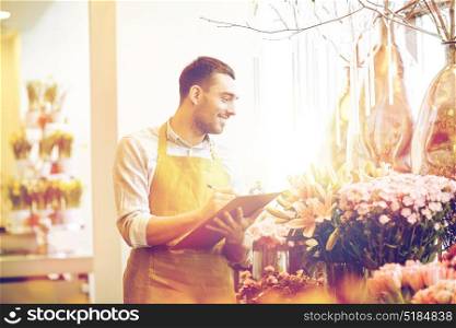 people, sale, retail, business and floristry concept - happy smiling florist man with clipboard writing and making notes order at flower shop. florist man with clipboard at flower shop