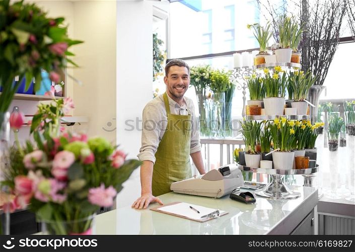 people, sale, retail, business and floristry concept - happy smiling florist man with clipboard and cashbox standing at flower shop counter