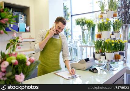 people, sale, retail, business and floristry concept - happy smiling florist man calling on smartphone and making notes to clipboard at flower shop counter