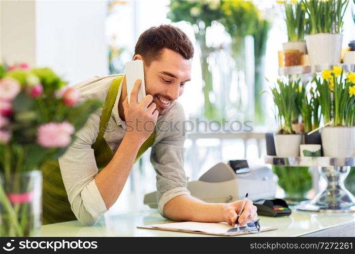 people, sale, retail, business and floristry concept - happy smiling florist man calling on smartphone and making notes to clipboard at flower shop counter. florist man calling on smartphone at flower shop