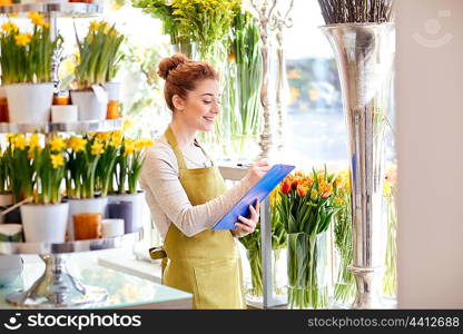 people, sale, retail, business and floristry concept - happy smiling florist woman with clipboard writing and making notes order at flower shop