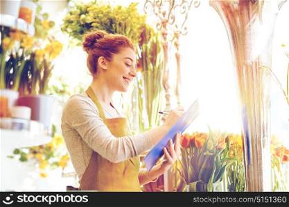 people, sale, retail, business and floristry concept - happy smiling florist woman with clipboard writing and making notes order at flower shop. florist woman with clipboard at flower shop