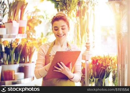 people, sale, retail, business and floristry concept - happy smiling florist woman with clipboard writing and making notes order at flower shop. florist woman with clipboard at flower shop