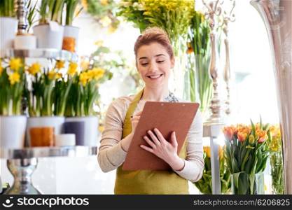 people, sale, retail, business and floristry concept - happy smiling florist woman with clipboard writing and making notes order at flower shop
