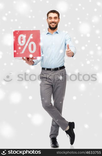 people, sale, shopping, christmas and winter holidays concept - smiling man holding red percentage sign showing thumbs up over snow background