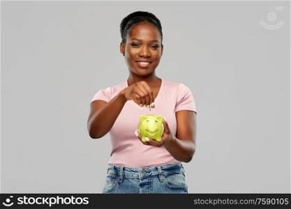 people, saving and finances concept - happy smiling african american young woman with piggy bank over grey background. happy african american woman with piggy bank