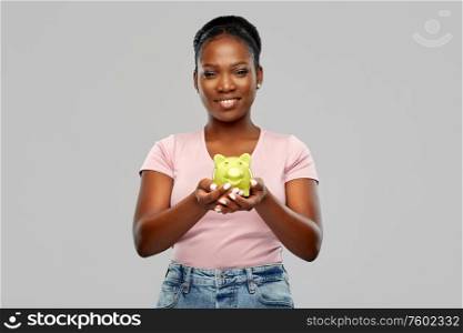 people, saving and finances concept - happy smiling african american young woman with piggy bank over grey background. happy african american woman with piggy bank