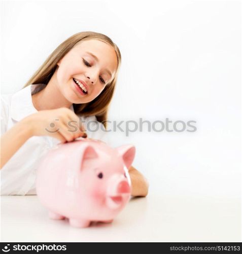 people, saving and finances concept - happy smiling girl putting coin into piggy bank. happy smiling girl putting coin into piggy bank
