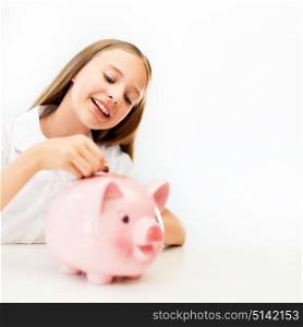 people, saving and finances concept - happy smiling girl putting coin into piggy bank. happy smiling girl putting coin into piggy bank