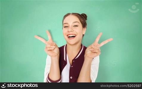 people, school, education and gesture concept - happy smiling pretty teenage student girl showing peace sign over green chalkboard background. happy student girl showing peace sign over green