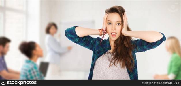 people, school, education and teens concept - pretty teenage student girl holding to head over classroom background with teacher and classmates