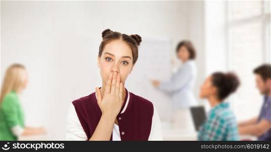 people, school, education, expression and teens concept - confused teenage student girl covering her mouth by hand over classroom background with teacher and classmates