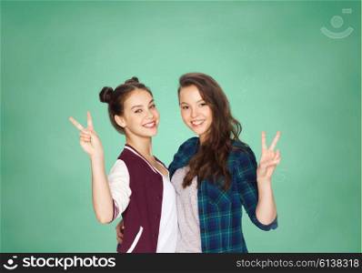 people, school, education, gesture and friends concept - happy smiling pretty teenage student girls hugging and showing peace hand sign over green chalk board background