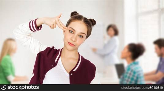 people, school, education, stress and teens concept - bored teenage student girl making headshot by finger gun gesture over classroom background with teacher and classmates