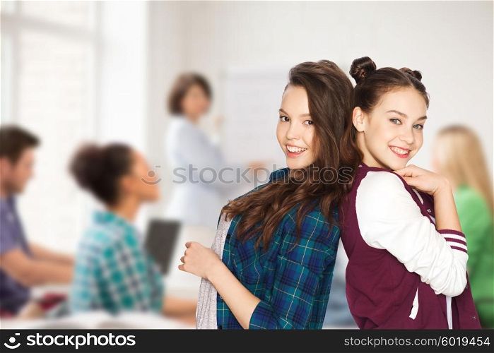 people, school, education, teens and friendship concept - happy smiling pretty teenage student girls over classroom background with teacher and classmates