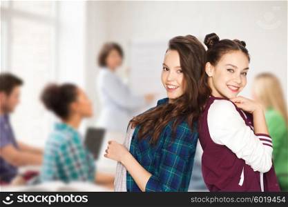 people, school, education, teens and friendship concept - happy smiling pretty teenage student girls over classroom background with teacher and classmates