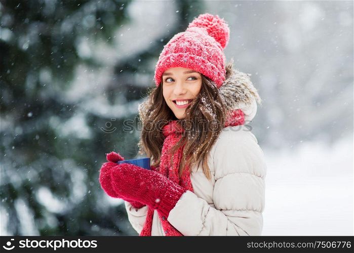 people, season and christmas concept - happy teenage girl or young woman with tea cup outdoors in winter park. happy young woman with tea cup in winter park