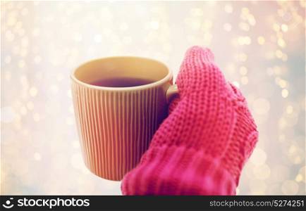 people, season and drinks concept - close up of hand in winter mitten holding tea mug outdoors. close up of hand in winter mitten holding tea mug