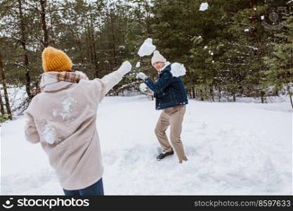 people, season and leisure concept - happy couple playing snowballs in winter park. happy couple playing snowballs in winter park