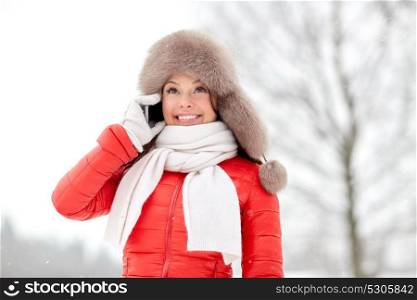people, season and leisure concept - happy smiling woman in winter fur hat calling on smartphone outdoors. happy woman in winter hat calling on smartphone