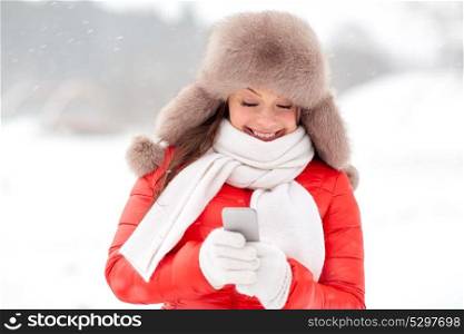people, season and leisure concept - happy smiling woman in winter fur hat with smartphone outdoors. happy woman in winter fur hat with smartphone