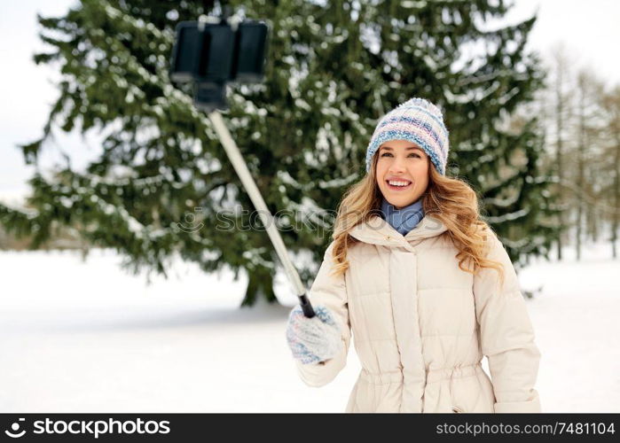 people, season and leisure concept - happy smiling woman taking picture by selfie stick in winter. woman taking picture by selfie stick in winter