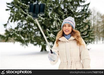 people, season and leisure concept - happy smiling woman taking picture by selfie stick in winter. woman taking picture by selfie stick in winter