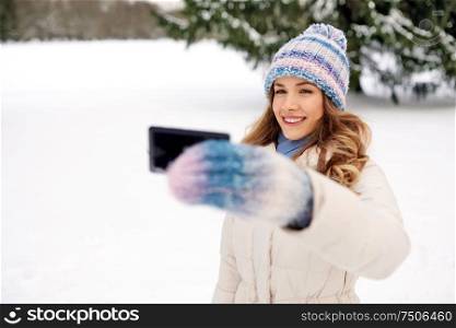 people, season and leisure concept - happy smiling woman taking selfie by smartphone in winter. woman taking selfie by smartphone in winter