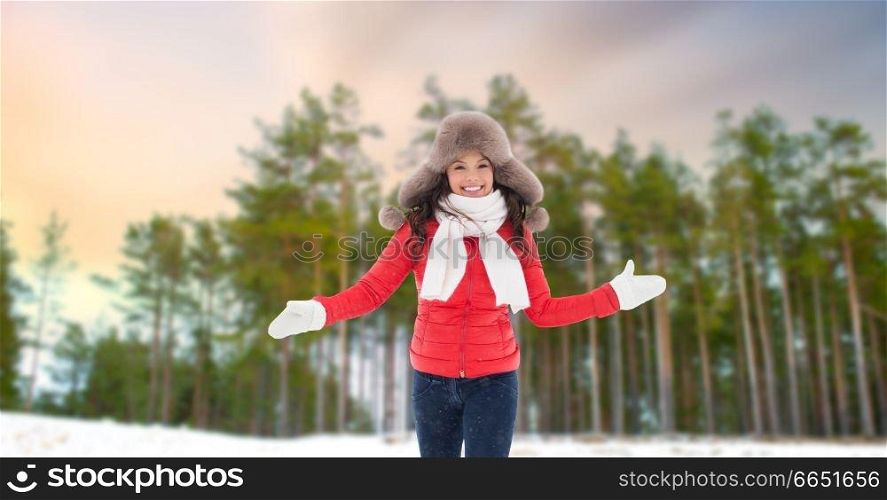 people, season and leisure concept - happy woman in fur hat outdoors over winter forest background. happy woman in fur hat over winter forest