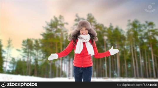 people, season and leisure concept - happy woman in fur hat outdoors over winter forest background. happy woman in fur hat over winter forest