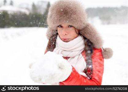 people, season and leisure concept - happy woman in winter fur hat blowing on snow in her hands outdoors. happy woman with snow in winter fur hat outdoors