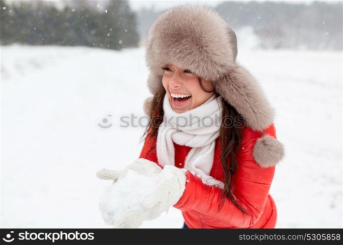 people, season and leisure concept - happy woman in winter fur hat holding snow in her hands outdoors. happy woman with snow in winter fur hat outdoors