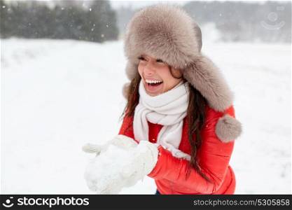 people, season and leisure concept - happy woman in winter fur hat holding snow in her hands outdoors. happy woman with snow in winter fur hat outdoors