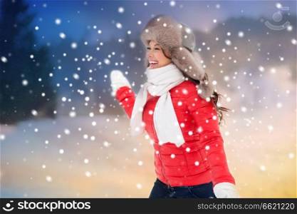 people, season and leisure concept - happy woman in winter fur hat having fun outdoors over evening background and snow. happy woman in winter fur hat having fun outdoors