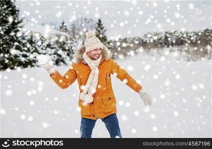 people, season and leisure concept - happy young man playing snowballs in winter