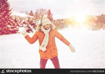 people, season and leisure concept - happy young man playing snowballs in winter