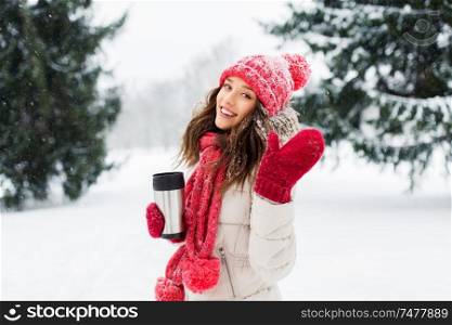 people, season, drinks and christmas concept - happy teenage girl or young woman with hot drink in tumbler outdoors in winter park and waving hand. young woman with hot drink in tumbler in winter