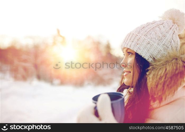 people, season, drinks and leisure concept - happy young woman with tea cup outdoors in winter